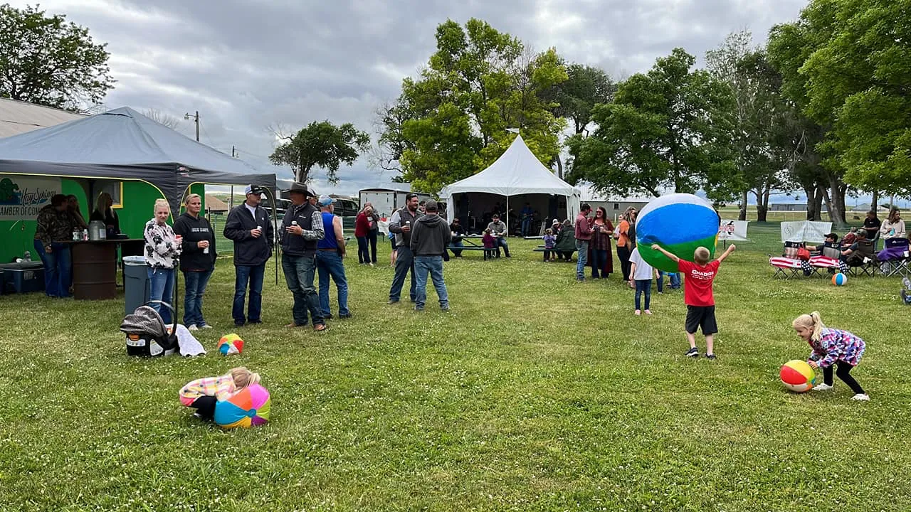 Families and children with beach balls at an outdoor tent gathering on the grass