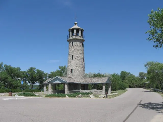 Stone lighthouse-style tower and picnic shelter under a clear blue sky