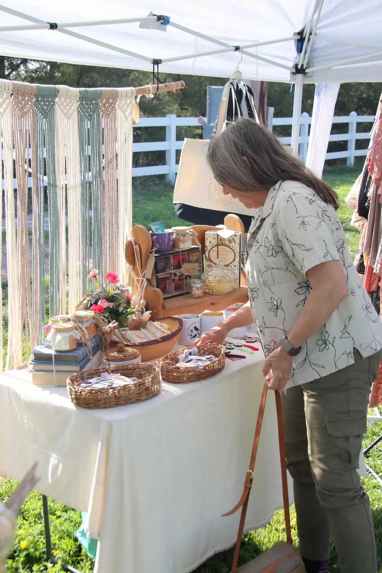 Woman browsing handmade macrame wall hangings and woven baskets under a white market tent