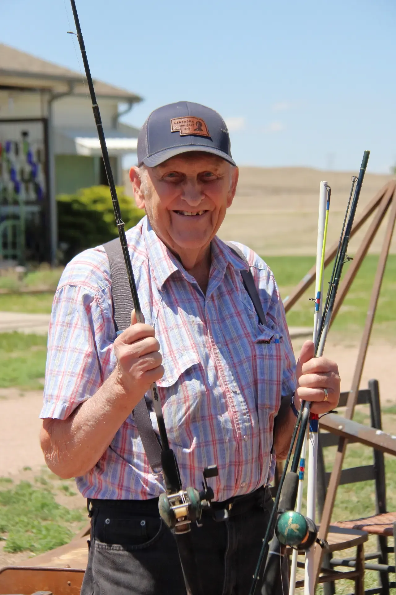 Smiling man in a Nebraska cap holding several fishing rods at an outdoor sale